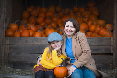 Portrait of smiling woman and daughter sitting against pumpkins