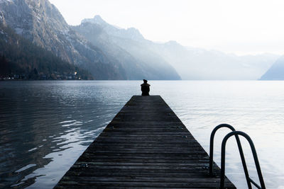 Rear view of man on pier over lake against sky