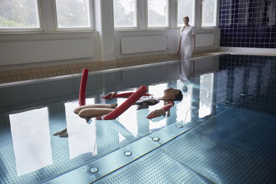 Full length of woman swimming with noodle floats in pool at rehabilitation center