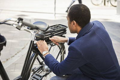 Young male commuter locking electric bicycle in city