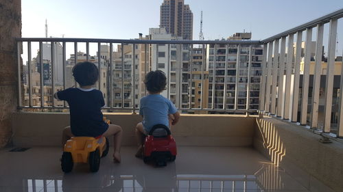 Rear view of boys sitting on toy vehicle at balcony in city