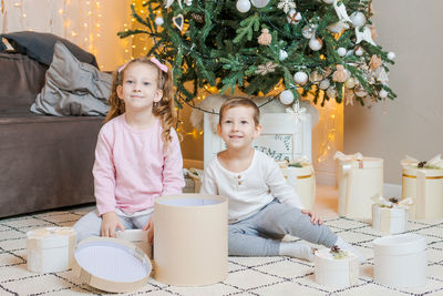 Caucasian brothers and sisters sit together on floor in their living room