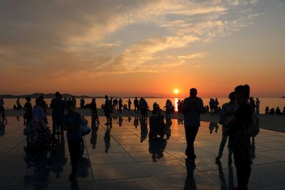 Silhouette people on shore against sky during sunset