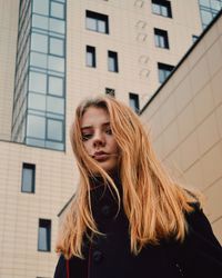 Low angle portrait of young woman against building in city