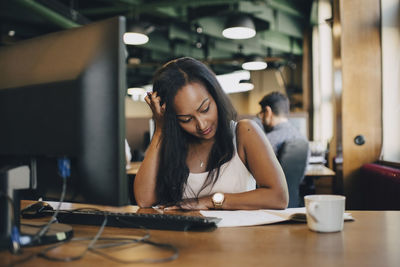 Businesswoman with hand in hair reading book at desk in office