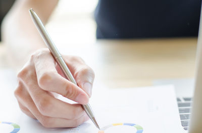 Cropped hand of businesswoman writing on document at desk