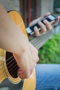 Midsection of woman playing guitar while holding mobile phone