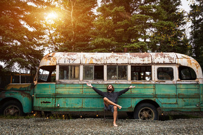Man with arms outstretched sitting against abandoned bus