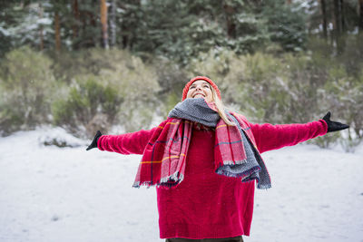 Cheerful woman with arms outstretched standing on snow covered land during winter
