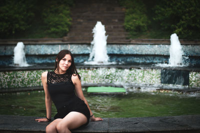 Portrait of young woman sitting against fountain