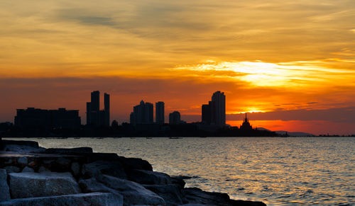 Sea by buildings against sky during sunset