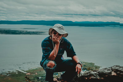 Man sitting on rock by sea against sky