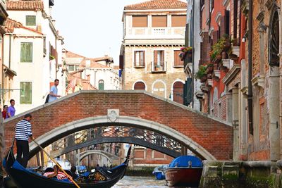 People in canal amidst city against sky