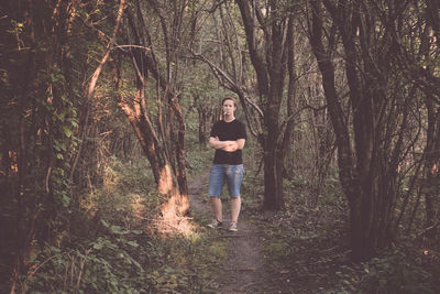 Full length portrait of young man standing with arms crossed in forest