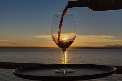 Close-up of wineglass against sea during sunset