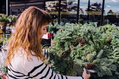 Young woman choosing a decorative green christmas wreath in store or on the market.