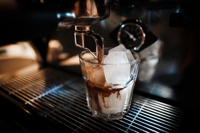 Close-up of coffee pouring in drinking glass at cafe