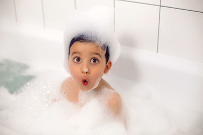 Boy with big eyes a caucasian child bathes in a white bath with foam