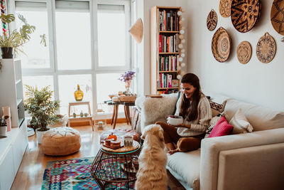 Woman holding food while playing with dog at home