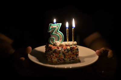 Piece of birthday cake with candles on plate being held