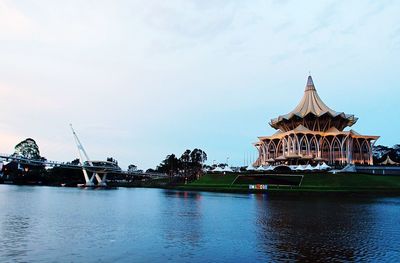 View of building by river against cloudy sky