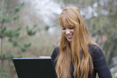 Young woman with long blond hair using laptop outdoors