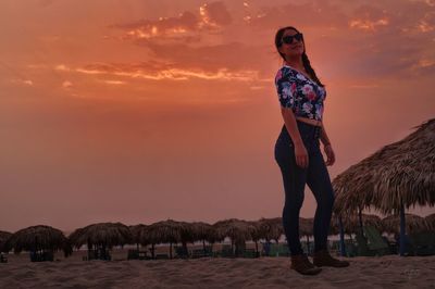 Woman standing on beach against sky during sunset