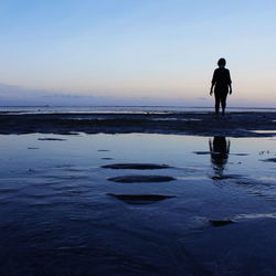 Silhouette woman standing on beach against sky during sunset