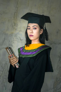 Portrait of young woman holding smart phone while standing against wall