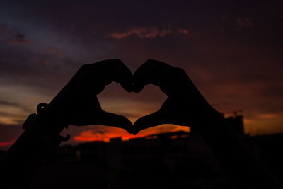 Silhouette woman holding heart shape against sky during sunset