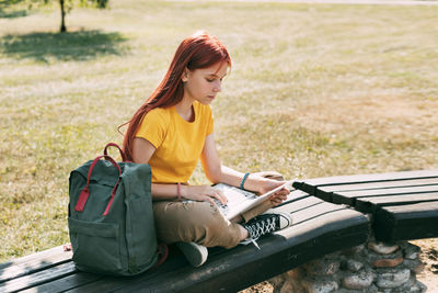 A teenage girl is sitting on a park bench with a laptop and preparing for lessons or exams. 