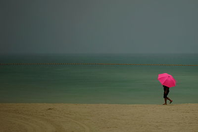 Rear view of woman standing on beach against clear sky