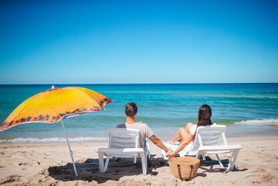 Rear view of woman sitting on beach against clear sky