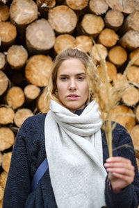 Portrait of young woman standing against logs