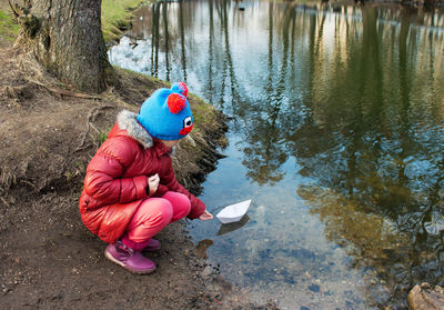 Side view of girl releasing paper boat in lake