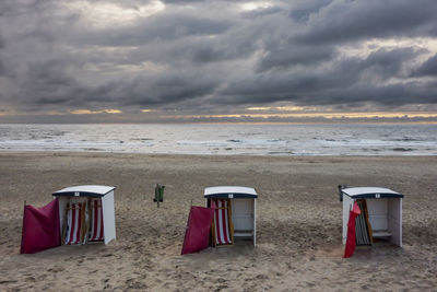 Empty chairs on beach against sky during sunset