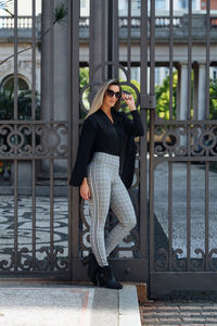 Portrait of woman wearing sunglasses standing against metal gate
