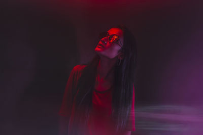 Young woman looking away while standing against black background
