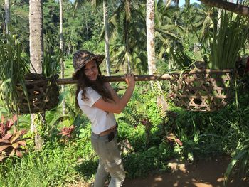 Portrait of smiling young woman carrying baskets while standing against plants