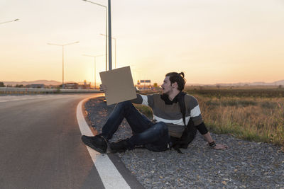 Man sitting by road against sky