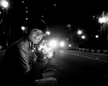 Portrait of young woman sitting on street at night