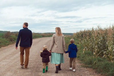 Family walking countryside road near corn field at autumn