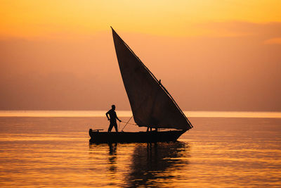 Silhouette man on sailboat in sea against sky during sunset