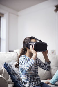 Girl using virtual reality simulator while sitting with sister at home