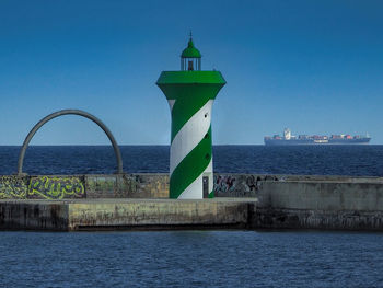 Lighthouse by sea against clear blue sky