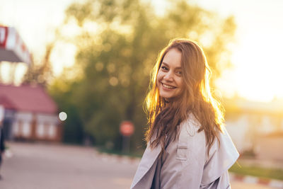 Beautiful smiling girl with long hair in a grey trench coat outdoors on the street spring