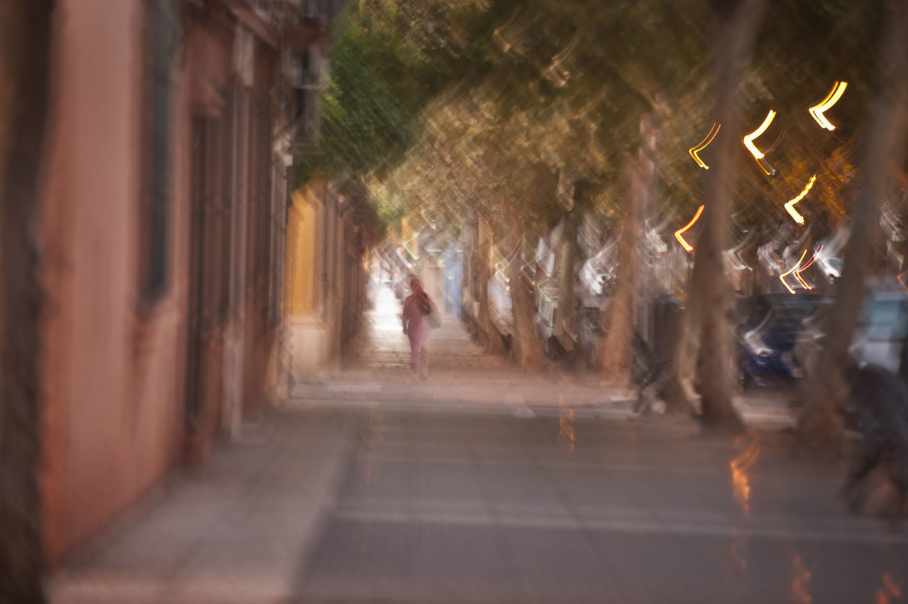 PEOPLE WALKING ON ILLUMINATED STREET AMIDST BUILDINGS