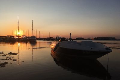 Sailboats moored in harbor at sunset