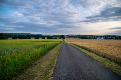 Diminishing perspective of empty road amidst agricultural field against cloudy sky