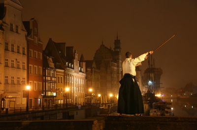 Rear view of man practicing martial arts while standing on retaining wall in city during sunset